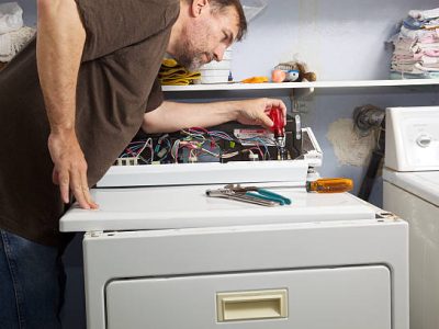 Homeowner repairman holds a screwdriver with other tools in hand to fix the non-heating gas dryer